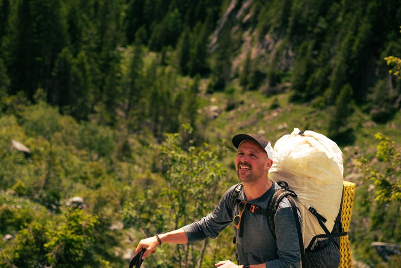 Der Outdoorguide Manuel Seiler ist ausser Atem beim Erklimmen eines Naturpfades im Wald bei Sonnenschein mit vollem Rucksack