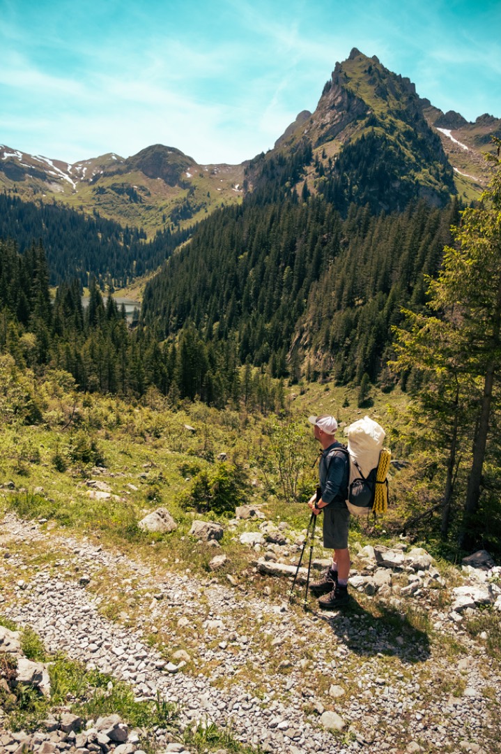 Manuel Seiler, Outdoorguide auf einem Bergwanderweg mit Wanderstöcken, Wanderschuhen und grossem Rucksack mitten in den Alpen